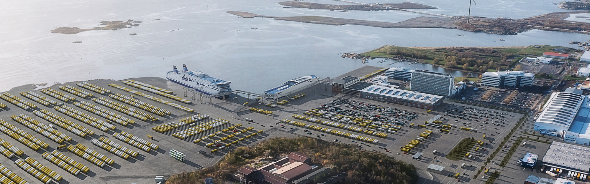 Flygfoto av hamnområde med fartyg, parkeringsplatser och byggnader vid vatten.