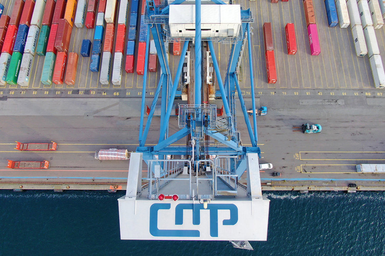Luftbild av containerkran med CMP-logotyp, containrar och hamnområde vid vatten.