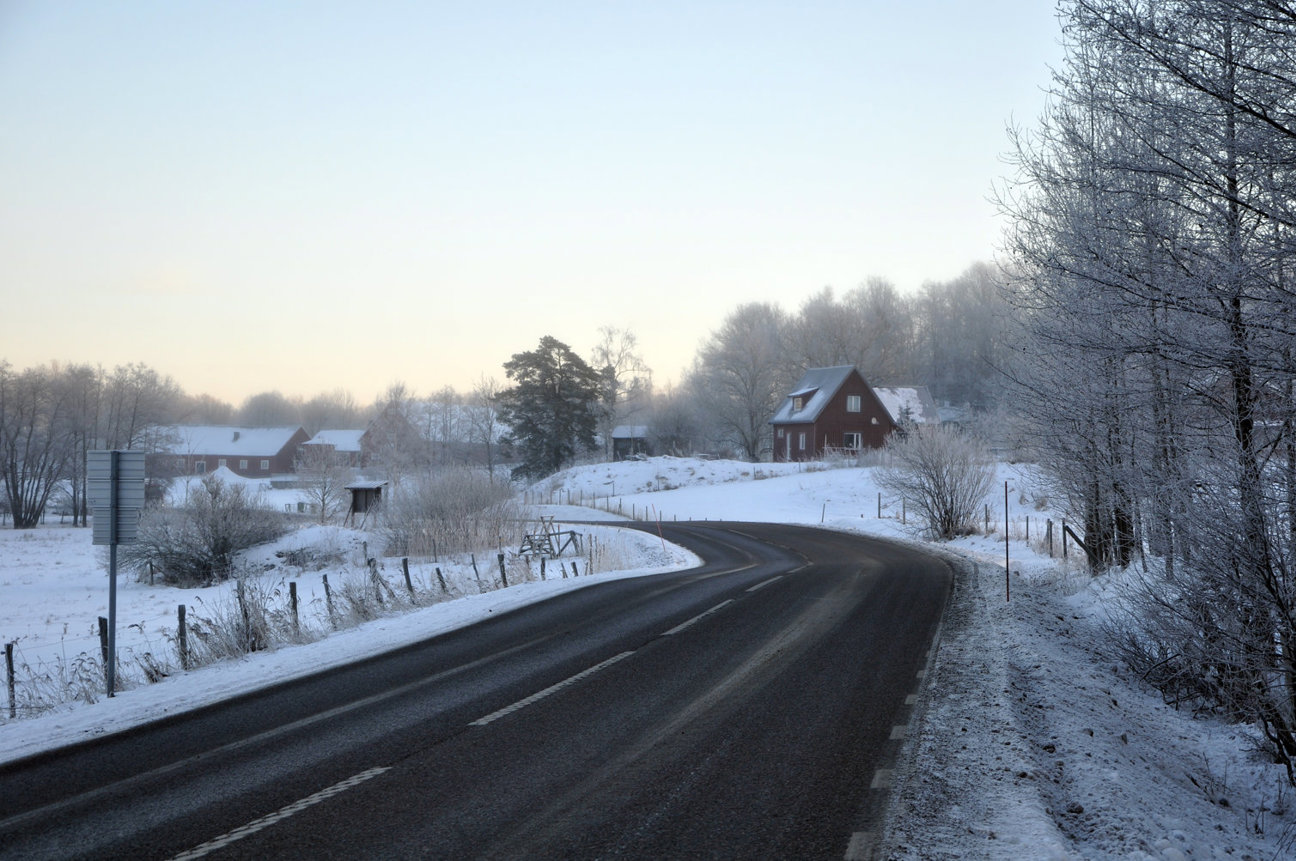 Snöig landsväg med röda hus och frostiga träd.