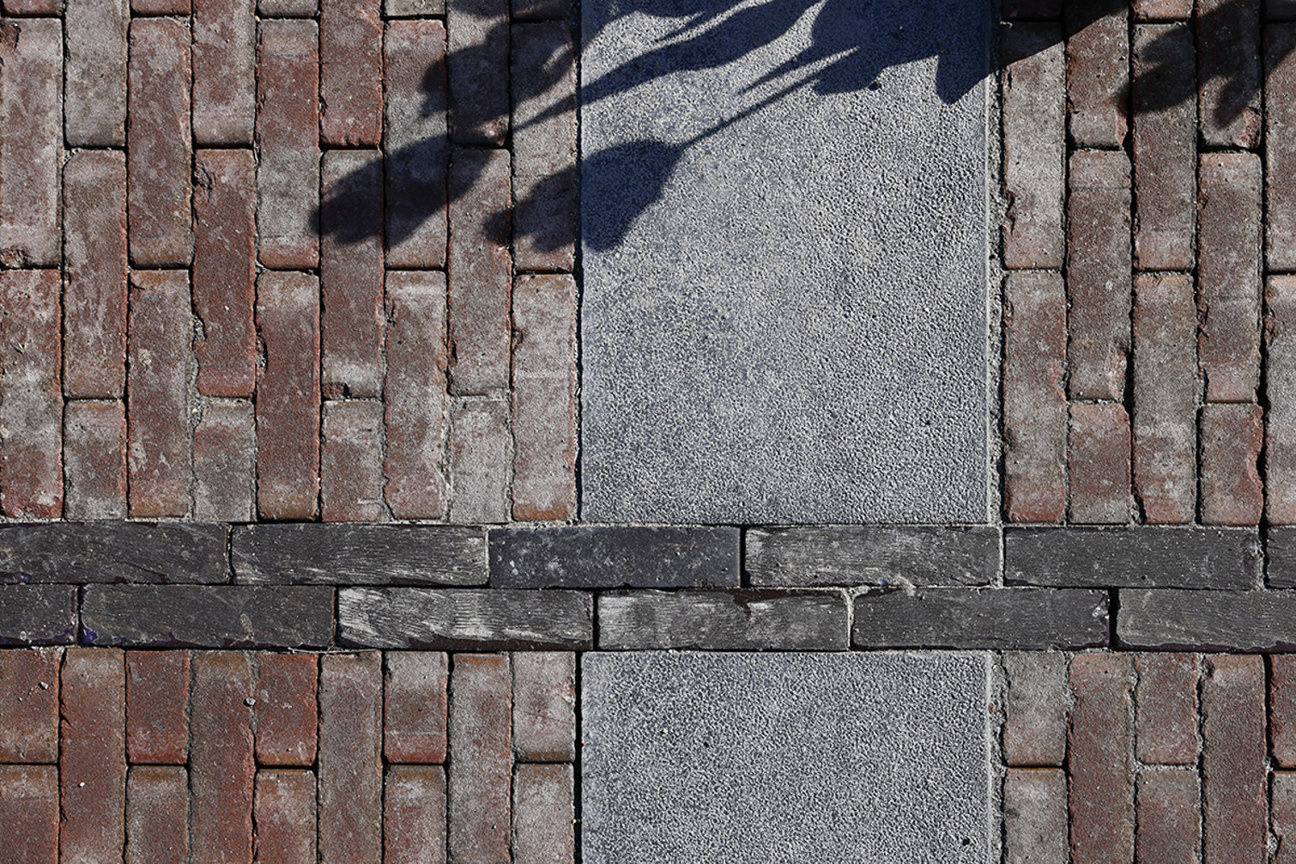 Röda tegelstenar och grå stenplattor med bladskuggor.