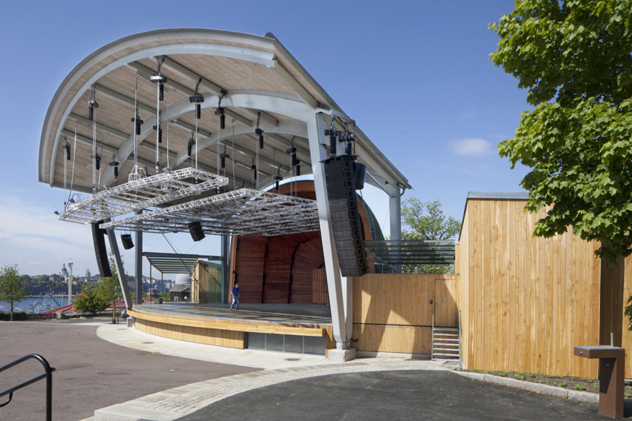 Utomhus-scen med takkonstruktion, ljudutrustning och en person på scenen.