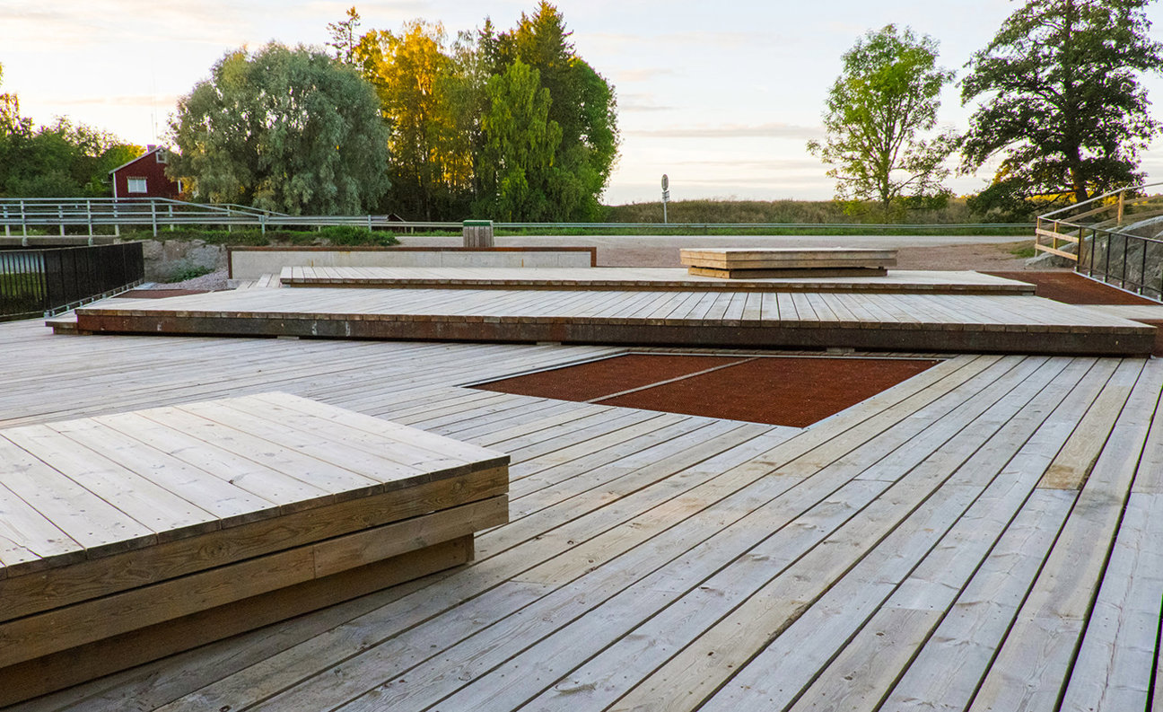 Trädäck med plattformar, träd och en röd byggnad i bakgrunden.