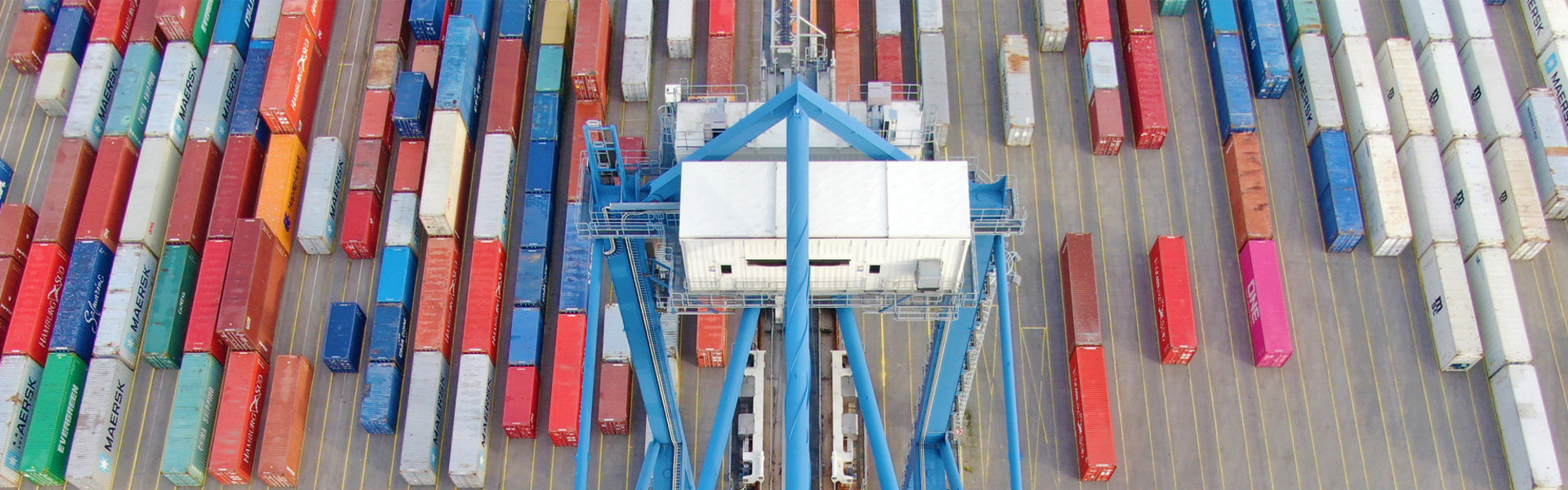 Färgglada containrar och en blå kran på en containerhamn.