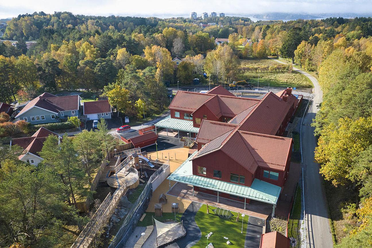 Flygfoto av hus med röda tak, träd och lekplats i ett bostadsområde.
