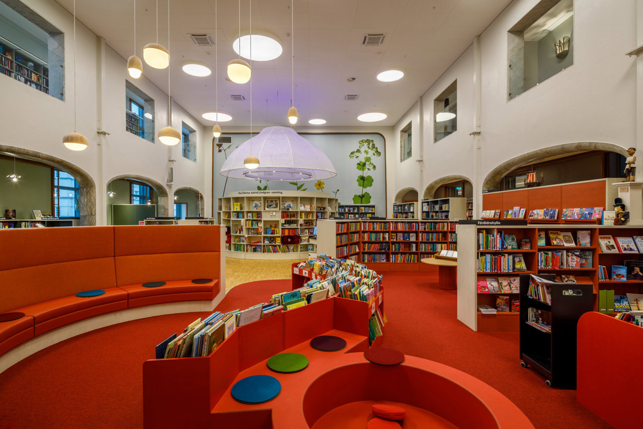 Biblioteksinredning med röda golv, orange soffor och bokhyllor fyllda med böcker.