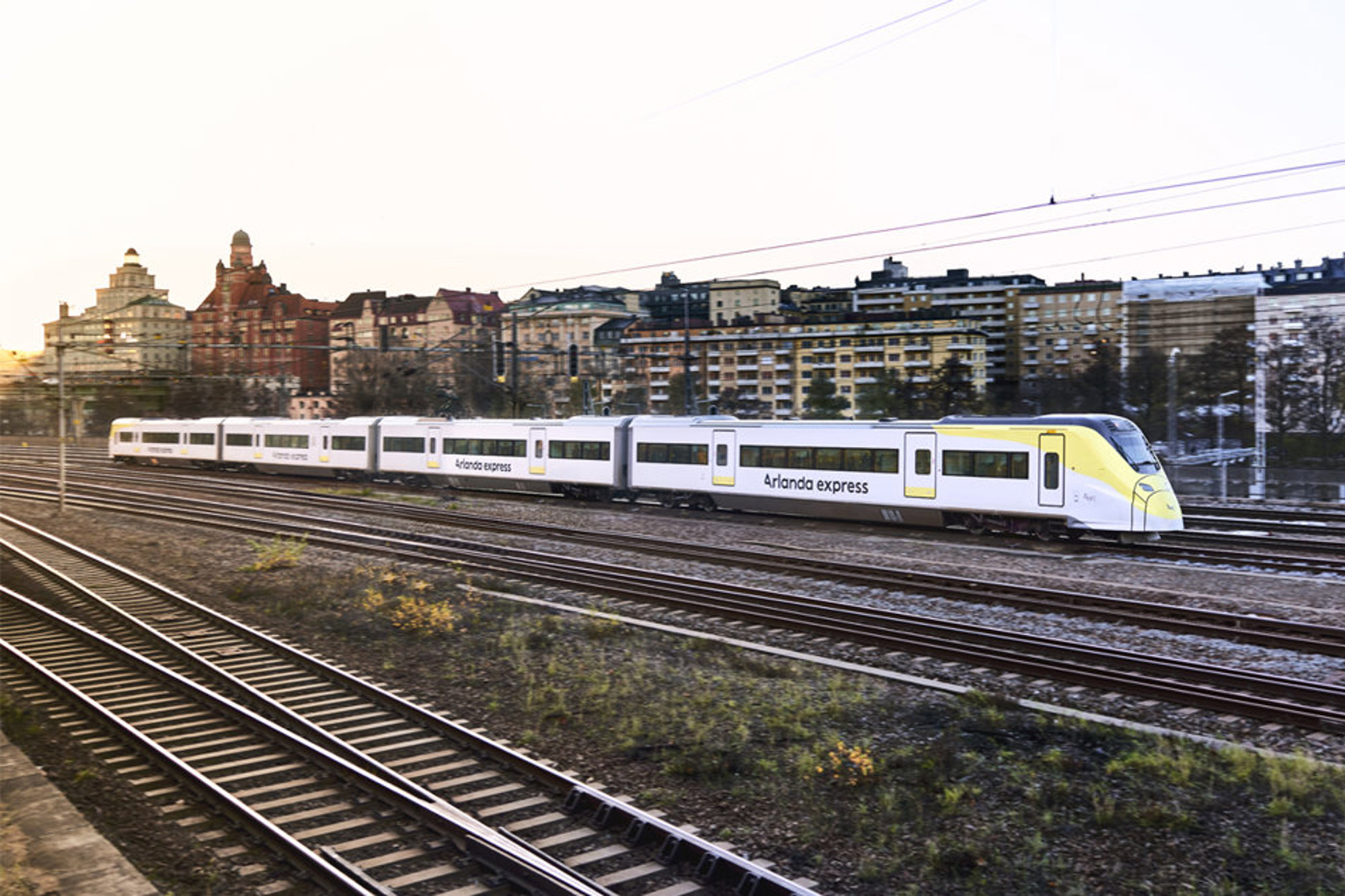 Arlanda Express-tåg på järnvägsspår med byggnader i bakgrunden.