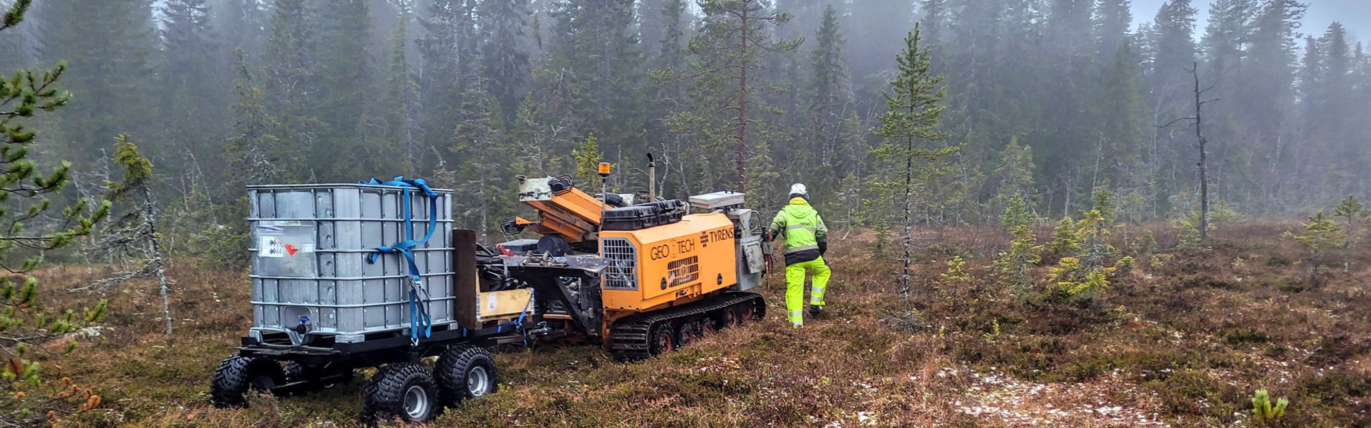Person i lysande grön arbetskläder bredvid maskin och behållare i skog.