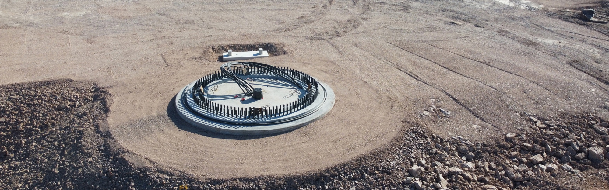 Cirkulär betongstruktur med rör på sandig och stenig markyta.
