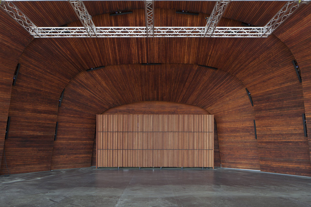 Inre av en byggnad med böjda träväggar, metallkonstruktioner ovanför och betonggolv.