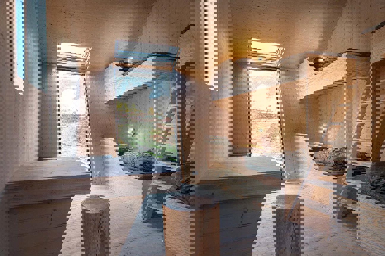 Inredning av en träbyggnad med över- och underbäddar, skrivbord och fönster mot utsikt.