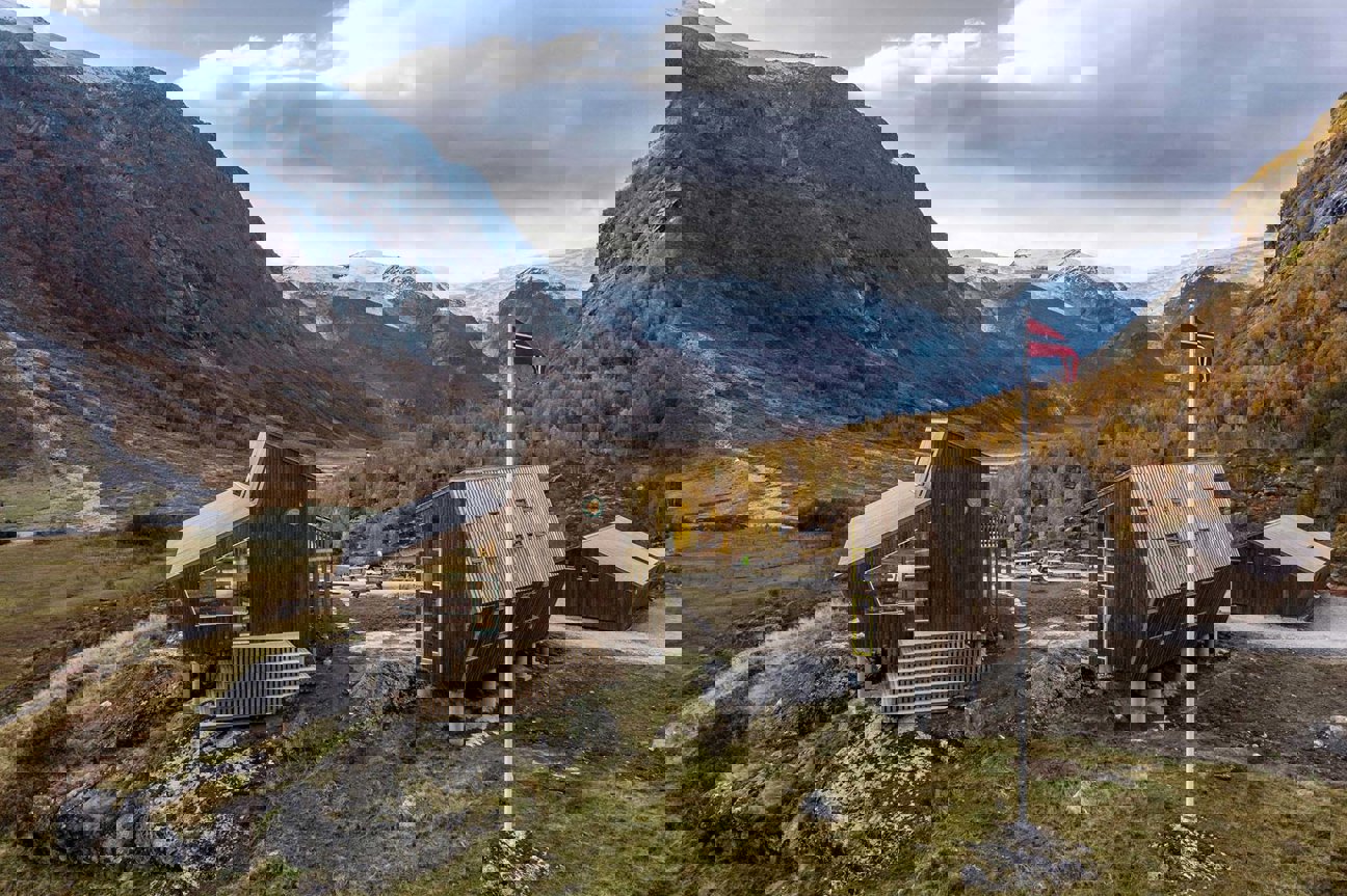 Moderna träbyggnader i en dalgång med snöklädda berg och en norsk flagga