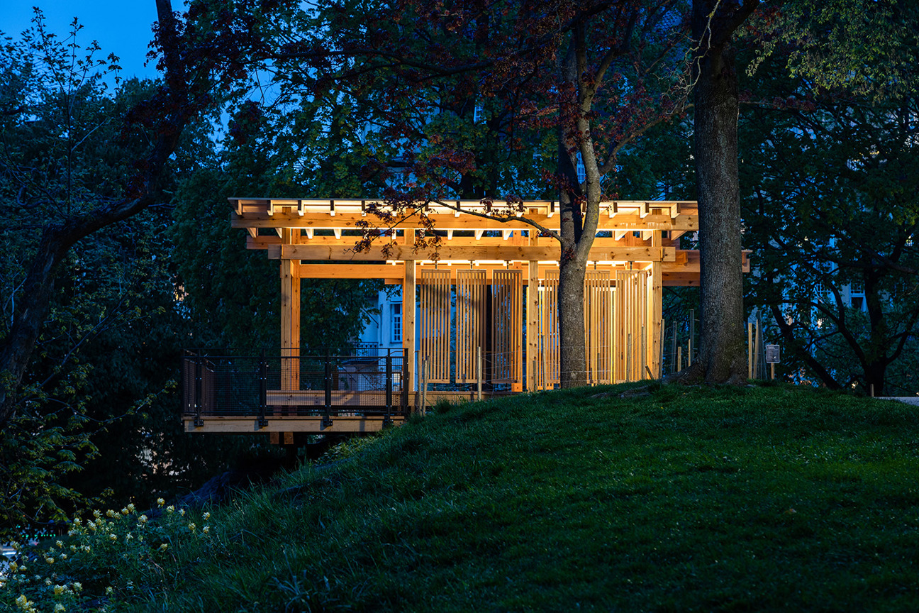 En träpaviljong med belysning omgiven av träd och gräs under kvällsskymning.