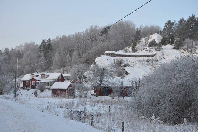 Snöigt landskap med röda hus, snötäckta träd och en backe.