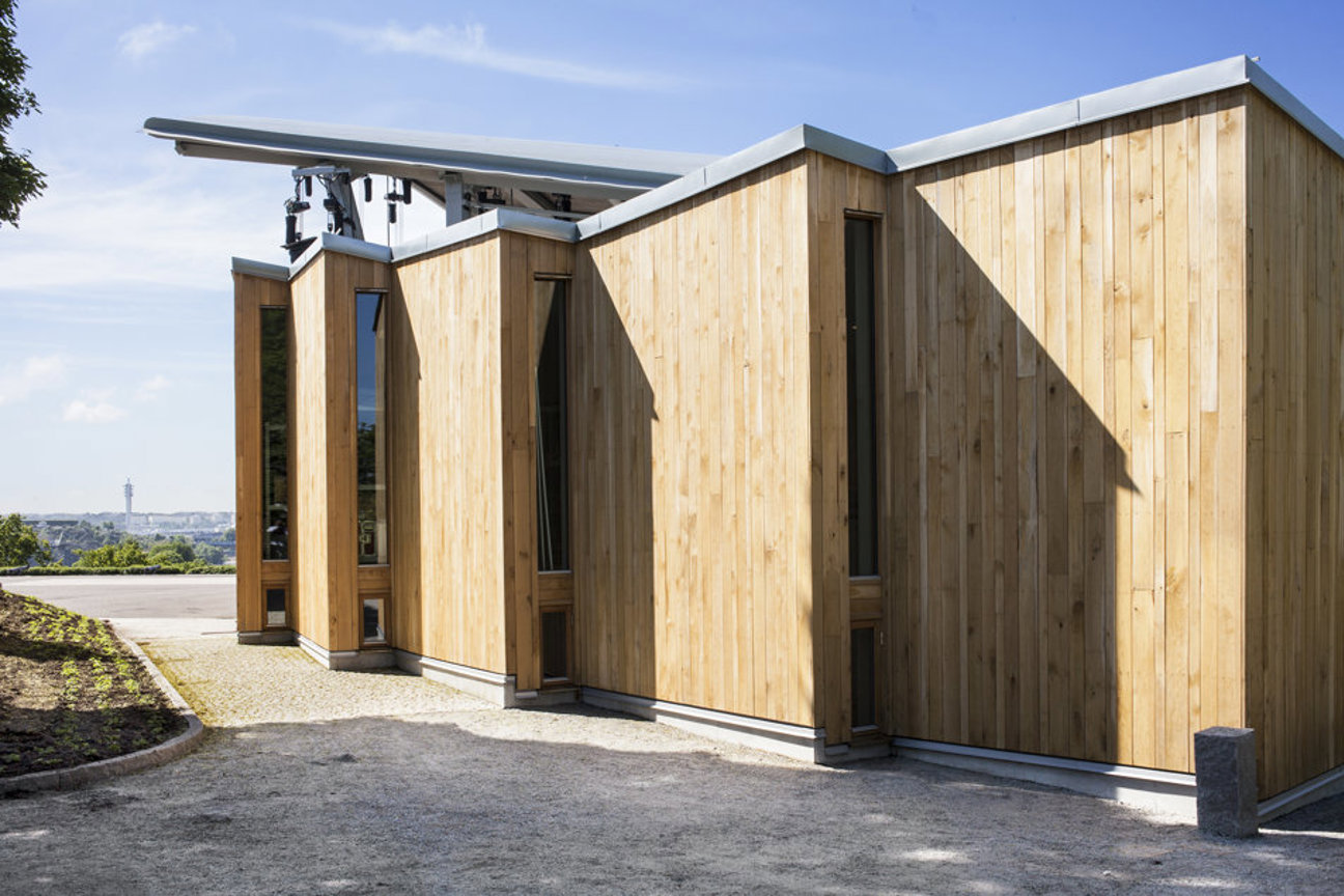 Modern träbyggnad med vertikala plankor och sluttande tak under klar himmel.